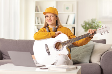 Poster - Young female sitting on a sofa at home with an acoustic guitar and a laptop computer