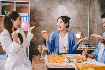 Bravo! A group of cheerful young people enjoy food and drink together in the office.