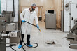 Middle age male working in industrial slaughterhouse and finishing his daily job. He is cleaning and washing food processing plant floor and machinery production lines with water.