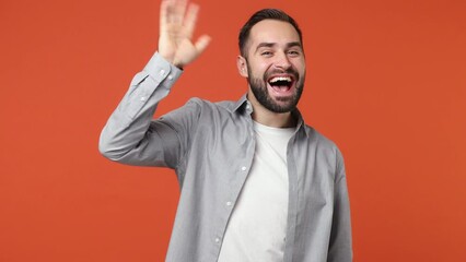 Wall Mural - Promoter young brunet man 20s years old wears blue shirt scream waving meet greet with hand as notices someone isolated on plain orange background studio portrait. People emotions lifestyle concept