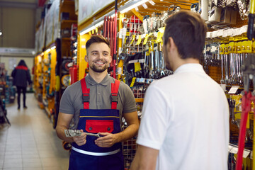 Wall Mural - Friendly shop assistant at DIY retail store helping customer choose tools and equipment. Happy smiling salesman helping young man who is buying wrenches and other tools for home repairs