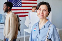 Waist Up Portrait Of Smiling Adult Woman At Voting Station Smiling At Camera With American Flag In Background, Copy Space