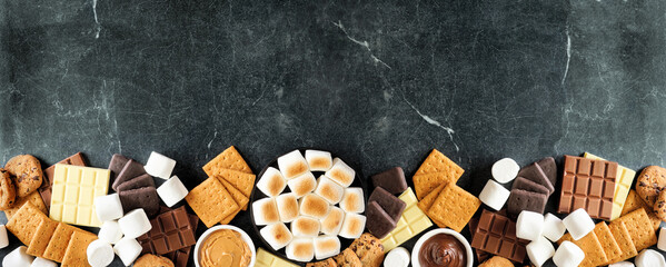 Poster - Smores buffet bottom border. Roasted marshmallows, crackers, chocolate and a assortment of ingredients. Top view over a dark stone background.