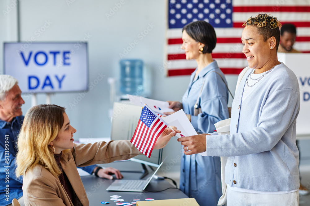 Side view portrait of smiling black woman taking ballot at voting station with American flag