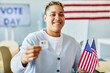 Waist up portrait of smiling person holding voting sticker and American flag on election day