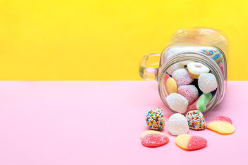 Colorful sweet different jelly candies in glass jar cup lying isolated on pink yellow background, pastry, confectionery, desserts. Tasty delicious unhealthy junk food