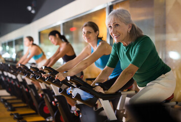 Portrait of confident adult woman training on fitness bike in gym indoor