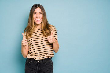 Wall Mural - Cute woman showing both thumbs up and looking excited in a studio