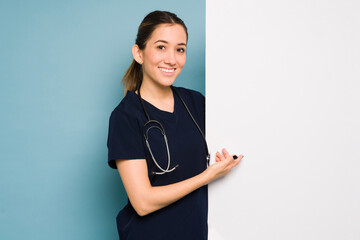 Wall Mural - Beautiful female doctor holding a white sign for copy in a studio with a blue background