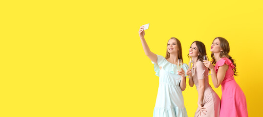 Sticker - Beautiful young women with glasses of champagne taking selfie on yellow background with space for text