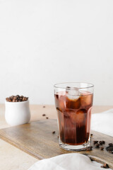 Wall Mural - Wooden board with glass of cold brew and coffee beans on table against light background