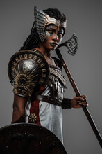 Shot Of Isolated On Grey Black Woman Warrior Holding Axe And Shield Dressed In Ancient Armor.