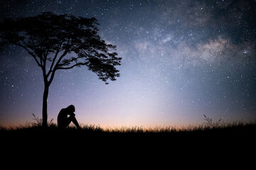 Wall Mural - The young man sat down alone under a large tree above a mountain meadow with beautiful night sky, star and Milky Way. He was tired, sad and disappointed.