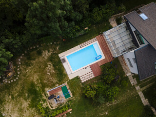 Wall Mural - Drone flight over beautiful green garden with pool and the wooden terrace of the pool is currently in progress