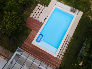 Wall Mural - Drone flight over beautiful green garden with pool and the wooden terrace of the pool is currently in progress