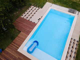 Wall Mural - Drone flight over beautiful green garden with pool and the wooden terrace of the pool is currently in progress