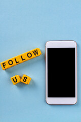 Vertical shot of smartphone and letter cubes. Isolated on blue background. Letter cubes saying follow us.