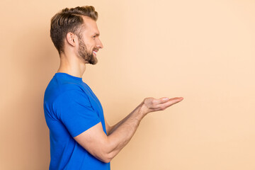 Wall Mural - Profile side photo of young man hold arms demonstrate promotion offer look empty space isolated over beige color background