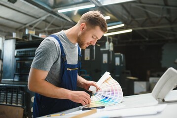 Portrait of production line worker controlling manufacturing process of modern packaging industrial machine in printing factory