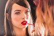Make-up Artist Applying Red Lipstick on the Full Natural Lips of a Beautiful Caucasian Woman With Cat Blue Eyes  Looking Away.