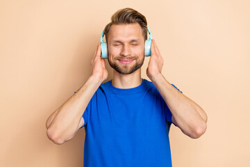 Poster - Photo of young guy good mood dreamy hands touch earphones sound isolated over beige color background