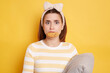 © sementsova321 - Image of young adult confused woman with dark hair keeps diet but eating cookie, posing isolated on yellow background,holding pillow and looking at camera, being upset and confused.