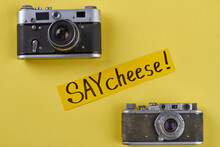 Two Vintage Photo Cameras On Yellow Background. Say Cheese Handwriting.