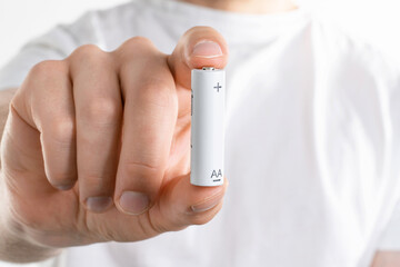 Close up image of mans hand holding battery on white background