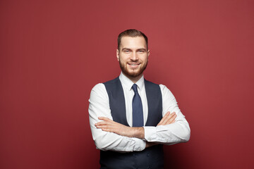 Wall Mural - Happy businessman standing with crossed hands and looking at camera on red background