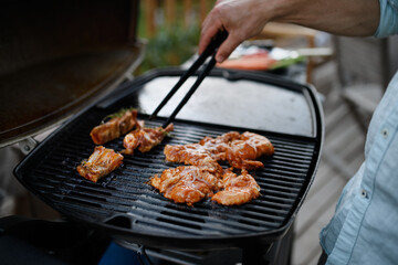 Wall Mural - Unrecognizable man grilling meat, ribs and wings, on grill during family summer garden party, close-up