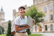 Cheerful asian schoolkid holding laptop and looking at camera outdoors.