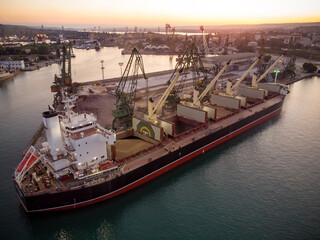 Wall Mural - Aerial view of big cargo ship bulk carrier is loaded with grain of wheat in port at sunset