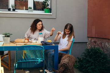 Wall Mural - mother and daughter feeding their dog while having breakfast in backyard