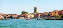 Cityscape Of Murano Island, Famous For The Production Of Artistic Glass. Sea Channel With Two Ferry Boats, Bell Tower Of The Cathedral, Basilica Of Saints Maria And Donato, VII Century. Venice, Italy.