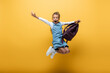 Excited schoolkid with backpack jumping on yellow background.