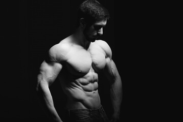 Wall Mural - Portrait of shirtless muscular man in a jeans. Young male hunk showing his perfect body and muscles on black background