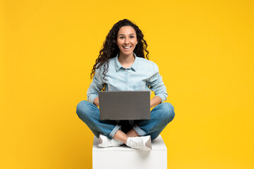 Poster - Full length of cheery young woman sitting cross legged with laptop, smiling at camera, working or studying online
