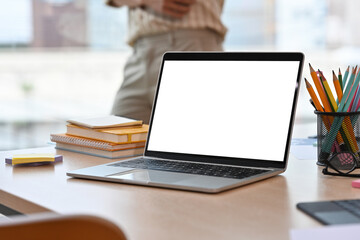Poster - Workplace desk with a laptop with a white blank screen, note books, pencils and a person in a background, for business and technology concept.