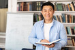 Korean Male Teacher Holding Book Standing Near Whiteboard In Classroom