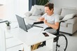 © Serhii - Freelancer in wheelchair using laptop near notebook and papers on table