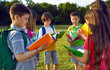 © Studio Romantic - Group of elementary school students read books together standing in circle in park near school. Smiling preteen boys and girls with colored books and with backpacks study together in park on sunny day