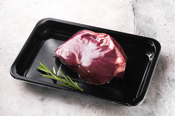 Wall Mural - Beef steak. Fresh raw beef steak with fork and rosemary in vacuum black plastic pack on grey stone background. Vacoom package. Top view. Mockup for design idea.