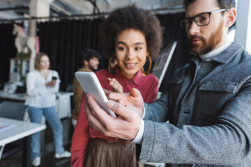 Wall Mural - advertising manager in eyeglasses showing mobile phone to african american woman.