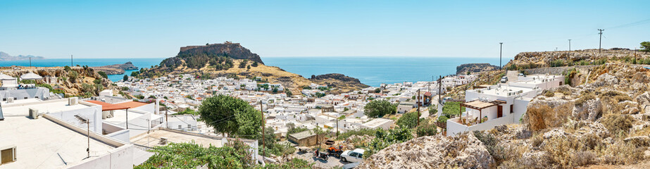 Old Lindos city on rocky hills overlooking Acropolis. White houses with private gardens scattered on island hills on Mediterranean coast