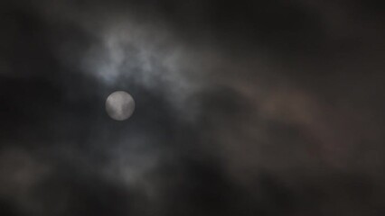 Wall Mural - Eerie dark and stormy sky with bright orb, sun or moon, shining bright as thick clouds pass.