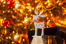 Deer Toy On Piano With Christmas Tree With Bright Lights On The Background. Christmas Atmosphere