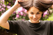 © PeterPike - Young beautiful smiling girl in a black T-shirt against the background of a blooming rhododendron touches her hair