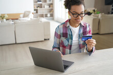 African American Teen Girl Holds Banking Credit Card, Shopping Online At Laptop At Home. E Commerce