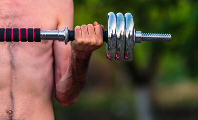 Nerd guy raising a dumbbell, Weak man lift a weight, dumbbells, biceps, muscle, fitness., tanned only on the hands, in nature garden