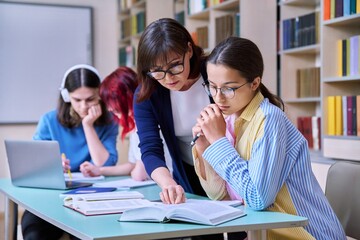 Group of teenage students and teacher study at desk in library